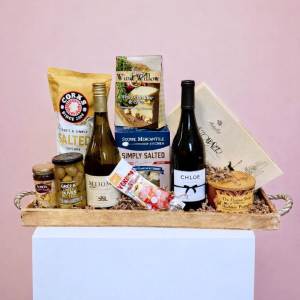 Gourmet gift tray with two wine bottles, popcorn, crackers, olives, and assorted snacks.