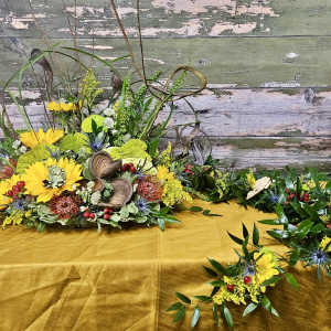 Yellow floral arrangement with greenery and decorative pods on a table
