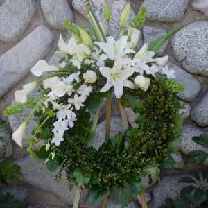 White floral wreath on a stand with lilies, calla lilies, and orchids