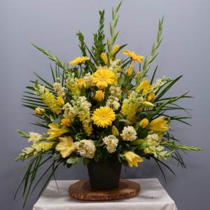 Yellow floral arrangement in a black pot with tall greenery