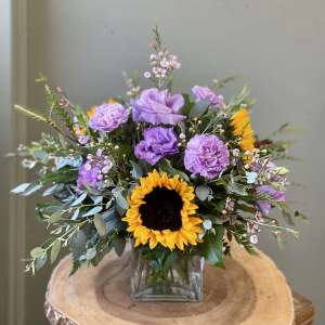 Sunflower and purple floral arrangement in a square glass vase
