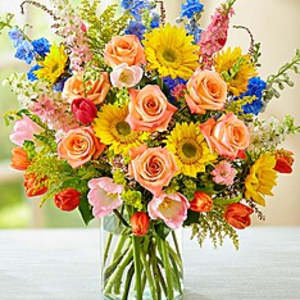 Mixed bouquet of roses, sunflowers, and tulips in a glass vase