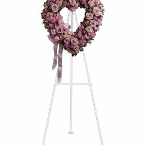 Heart-shaped standing wreath of pink and lavender roses and mixed flowers with a satin ribbon bow.