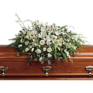White lily and rose casket spray arranged on a polished wooden casket