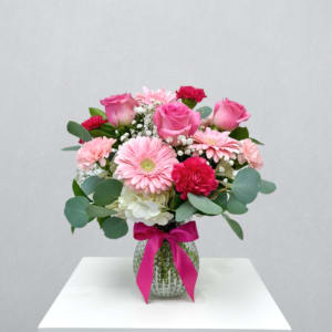 Pink roses, gerbera daisies and carnations in a clear vase with bright ribbon