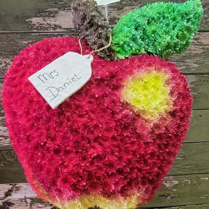 Apple-shaped floral arrangement in pink, green, and yellow with a name tag