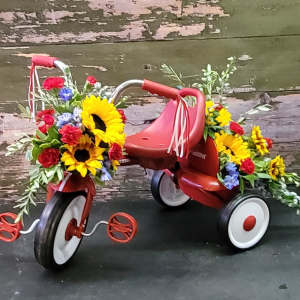 Flower-covered red tricycle with sunflowers and mixed blooms