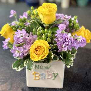 Yellow roses and lavender flowers in a white vase labeled New Baby