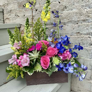 Bright mixed flower arrangement in a rectangular box with butterfly picks