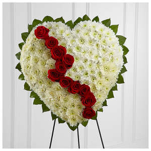 Heart-shaped funeral spray of white flowers with red roses on a stand