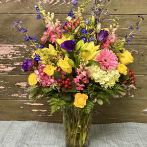 Mixed bouquet in a clear glass vase with yellow, pink, purple, and blue flowers
