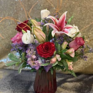 Mixed bouquet of roses, lilies, and purple flowers in a red vase