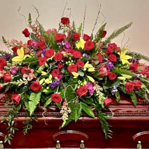 Large red and yellow floral casket spray on a wooden casket