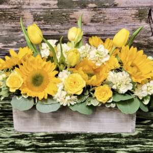 Yellow tulips, sunflowers, and white flowers in a rectangular wooden box