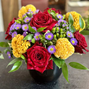 Bouquet of red roses, purple daisies, and yellow blooms in a black vase