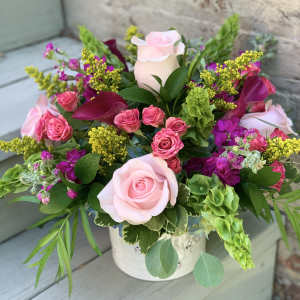Pink roses and magenta flowers arranged in a white container