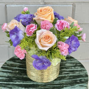 Peach roses, pink carnations, and purple lisianthus in a gold vase