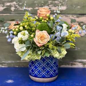 Mixed bouquet of peach roses, white blooms, and blue flowers in a patterned blue vase
