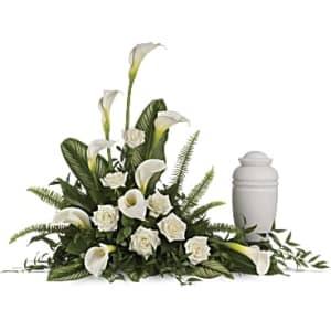 White calla lilies and roses arranged beside a white memorial urn