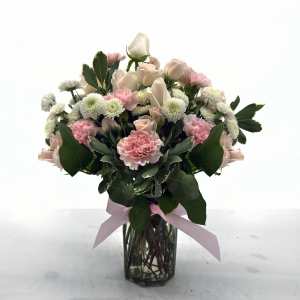 Pink roses and carnations arranged in a glass vase with a ribbon