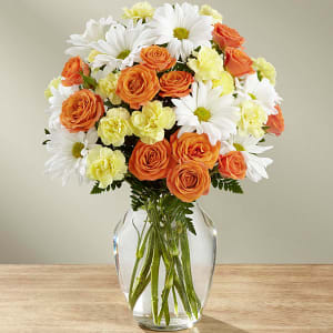 Bouquet of orange roses, white daisies, and pale yellow carnations in a glass vase