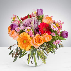 Mixed bouquet of roses, gerbera daisies, tulips, and daisies in a glass vase
