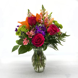 Mixed bouquet of roses, lilies, and purple flowers in a glass vase