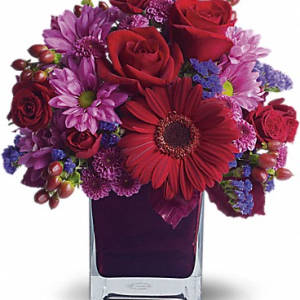 Red roses and purple flowers arranged in a square glass vase