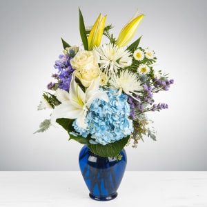 Mixed bouquet in a blue glass vase with white lilies, blue hydrangea, and yellow blooms