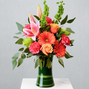 Bright bouquet of lilies, gerbera daisies, roses and carnations in a tall green glass vase