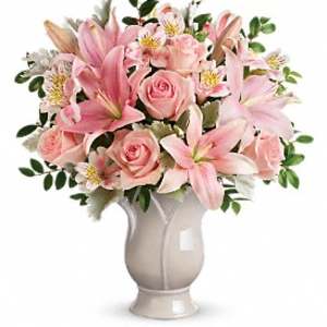 Pink lilies, roses, and alstroemeria arranged in a pale ceramic vase