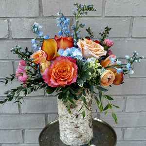 Colorful bouquet with roses, calla lilies, and blue flowers in a birch vase