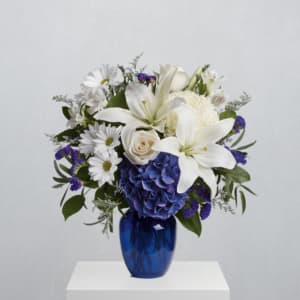 White lilies, blue hydrangea, and daisies arranged in a blue vase