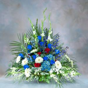 Large floral arrangement with blue, red, and white flowers in a low container