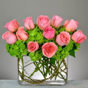 Pink roses arranged with green hydrangeas in a clear glass vase