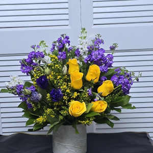 Yellow roses and purple flowers arranged in a gray vase