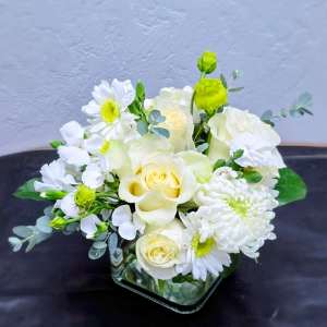 White and pale yellow floral arrangement in a square glass vase