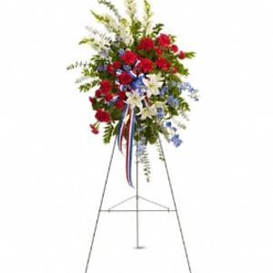 Tall red, white, and blue standing spray with lilies and carnations on a metal easel.