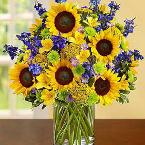 Sunflower bouquet in a clear glass vase with blue and green accent flowers