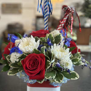 Red roses and white chrysanthemums in a patriotic striped container with blue and red ribbons