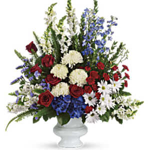 Tall red, white, and blue flower arrangement with roses and daisies in a white urn.