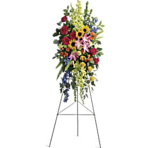 Tall standing spray with red roses, pink lilies, sunflowers and mixed blooms on a metal easel.