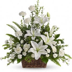 White lilies and carnations arranged in a wicker basket with lush ferns.