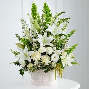 White lilies and roses in a white basket with tall green accents