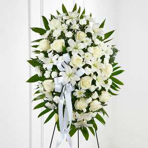 White floral standing spray with roses and lilies on a white ribboned easel