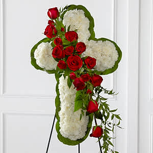 Cross-shaped floral tribute with red roses and white blooms on a stand