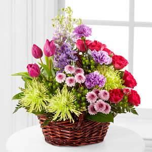 Mixed bouquet in a wicker basket with pink, purple, red, and green blooms