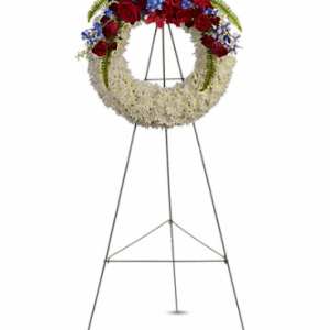 Standing floral wreath with red roses, blue flowers, and white blooms on an easel
