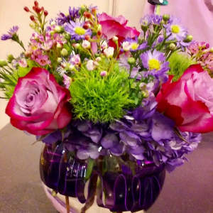 Bouquet of pink roses, purple daisies, and green filler in a round vase