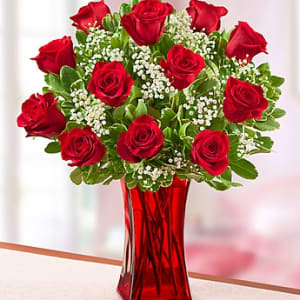 Red roses arranged in a red glass vase with white filler flowers